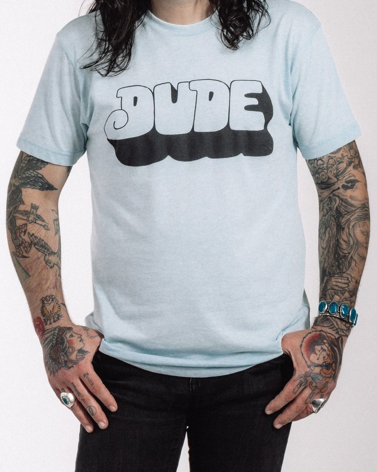 Light blue t-shirt with bold retro-style ‘DUDE’ lettering, Dude Cervantes merch
